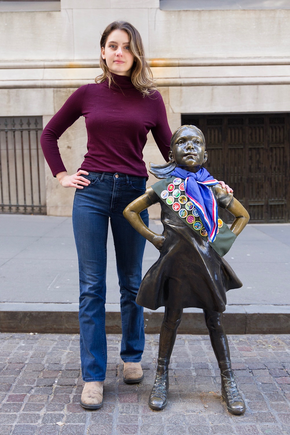 Sydney standing beside the Fearless Girl statue, wearing a scout sash of merit badges